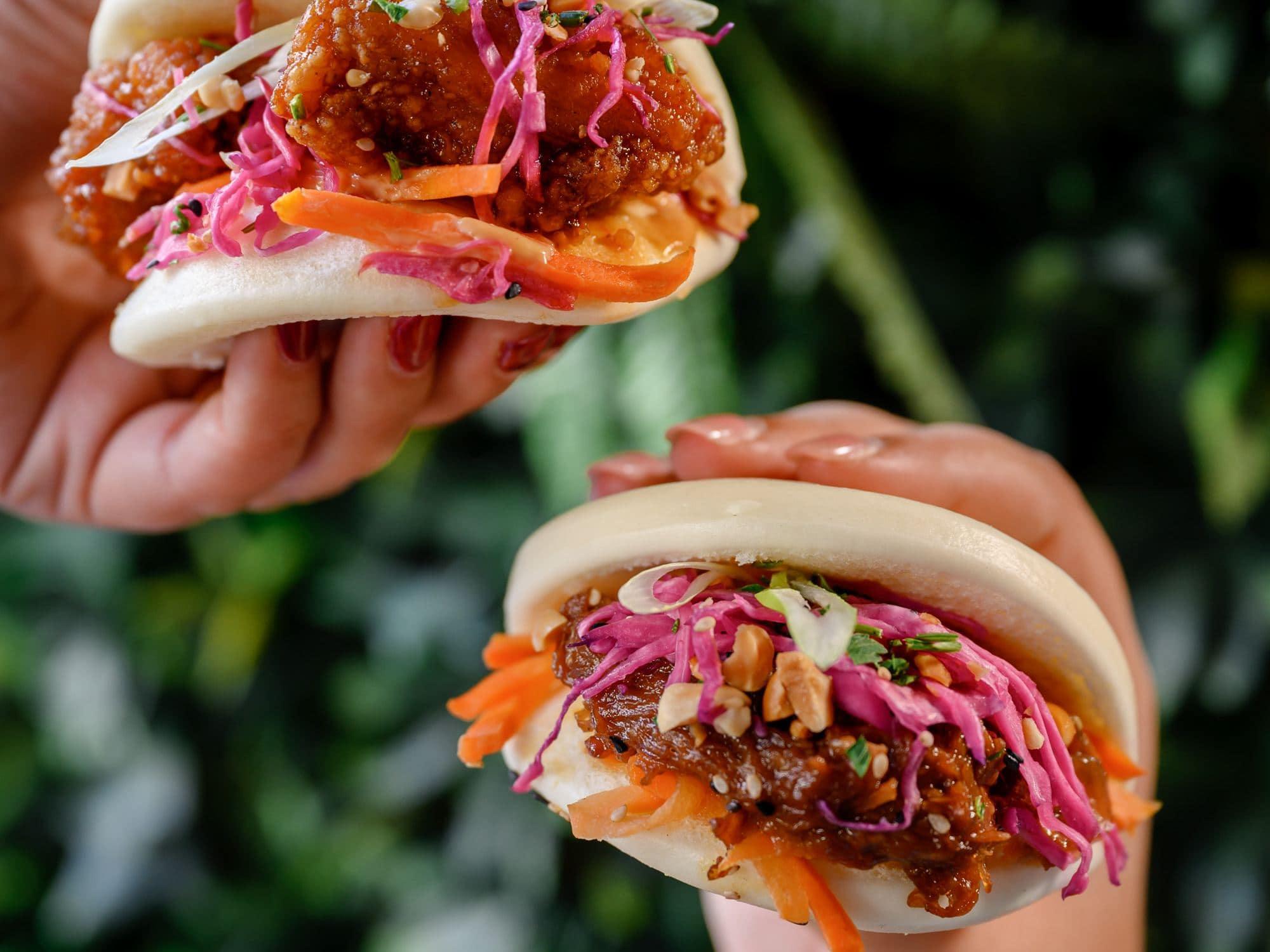 Two bao buns held up at Saigon Malta — satay pulled pork and bang bang chicken